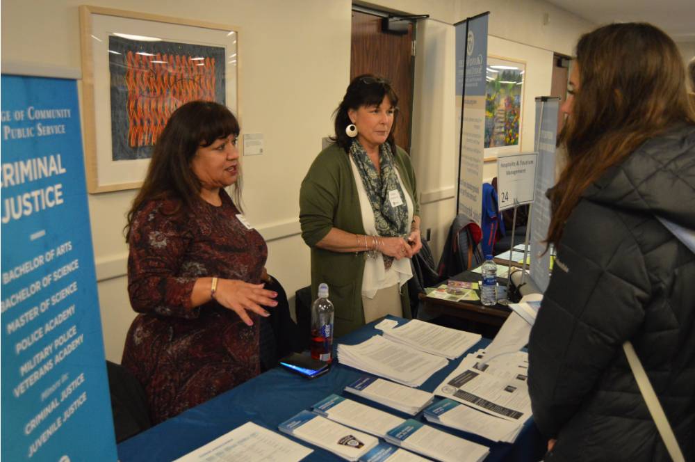 An alumna and a faculty member talk to a student about their field of study at the Academic Major Fair.